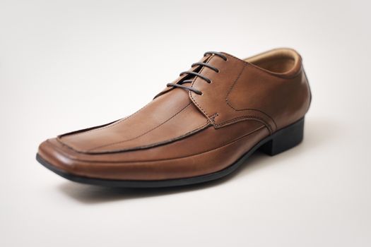 Men's brown leather shoe on light brown background. Very short depth-of-field.