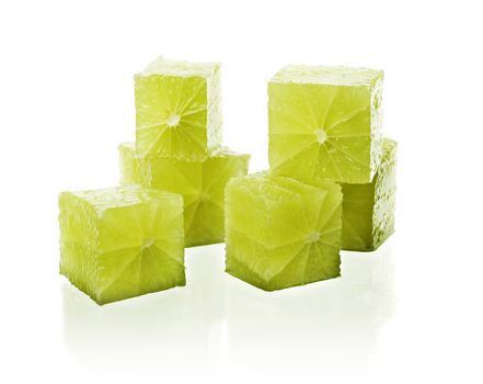 Real lime fruit cut into cubes on reflective white background.