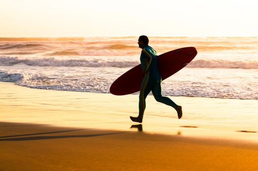 Surfer running on the beach with the waves at sunset in Portugal.