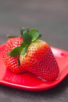 red juicy strawberry in red plate on a wooden surface