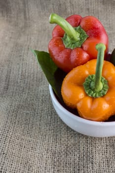 Orange and red sweet pepper with leaves on a Sackcloth background