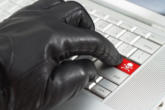 Hacker concept with hand wearing black leather glove pressing enter key button on a metallic laptop keyboard