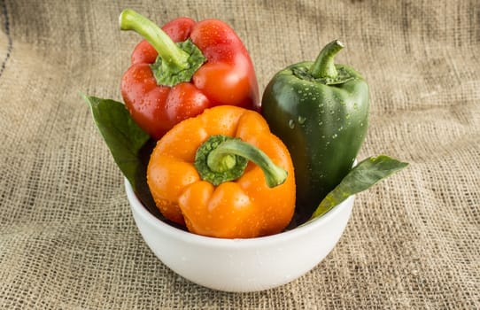 Orange, green and red sweet pepper with leaves on a Sackcloth background