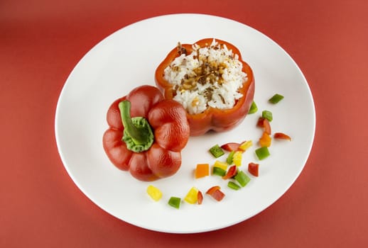 Stuffed red pepper in a dish on red background .