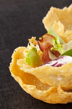 Cheese basket filled with fresh vegetable and bacon on black background. Culinary luxurious cheese eating. 