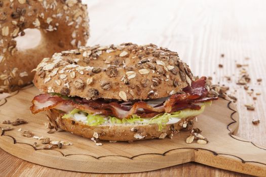 Whole grain bagel with bacon on wooden kitchen board on wooden background. Traditional bagel eating.