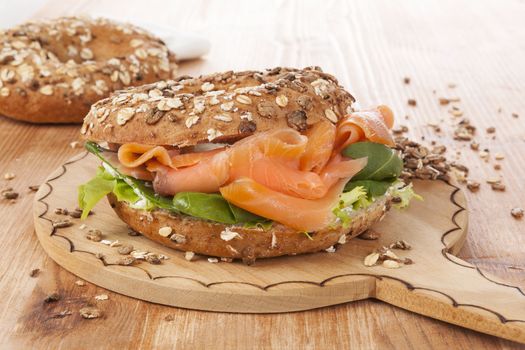 Salmon whole grain bagel on wooden kitchen board on wooden background. Traditional bagel eating.