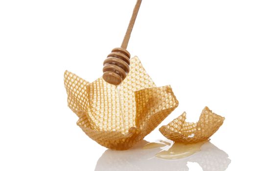 Honey dropping from wooden honey dipper onto honey comb isolated on white background. Organic honey background.