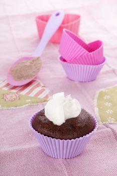 Modern contemporary baking background in purple and pink. Chocolate cupcake and baking forms with whipped cream on pink background. 