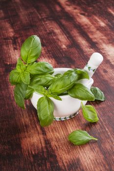 Fresh basil bunch in mortar with pestle on brown wooden background. Traditional cooking, rustic style.
