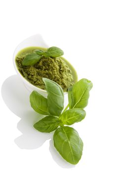 Green pesto with fresh basil herbs in white bowl isolated on white background. Culinary mediterranean eating.
