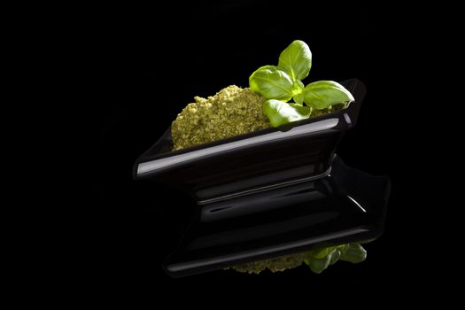 Organic green pesto with fresh basil leaves in black bowl isolated on black background. Culinary traditional pesto eating.