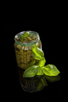 Green basil pesto isolated on black background. Culinary traditional mediterranean vegetarian eating.