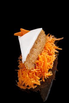 Delicious carrot cake on grated carrot isolated on black background with reflection. Culinary sweet dessert eating.