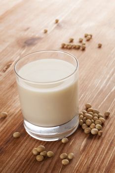 Soy milk in glass and soy crop on wooden background. Vegetarian and vegan eating concept. 