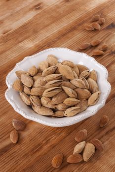 Almonds in white vintage bowl on wooden background. Healthy nuts eating.