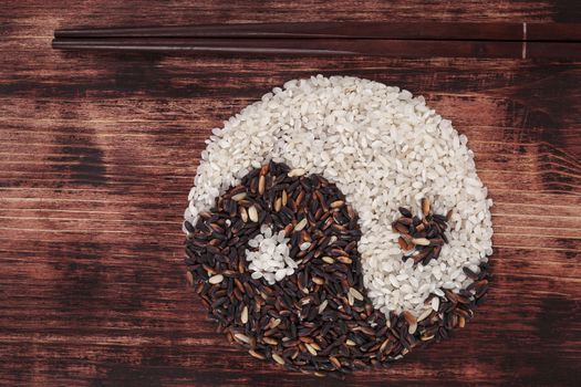 White and wild rice shaped as Yin yang symbol with chopsticks on dark wooden background. Asian culture.