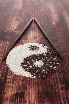 White and wild rice shaped as Yin yang symbol with chopsticks on dark wooden background. Traditional chinese eating and culture.