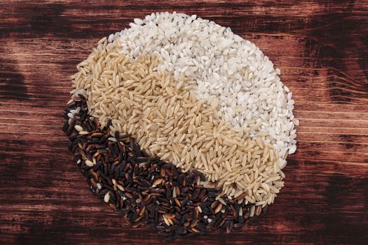 Different kinds of raw rice in circle shape on dark wooden background. White rice, brown rice and wild rice.