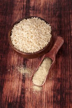 Rice in round wooden bowl with dietary rice fiber on wooden spoon on dark brown wooden background, top view. Healthy eating concept.