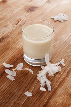 Glass of organic coconut milk with coconut flakes isolated on wooden background. Healthy vegan eating.
