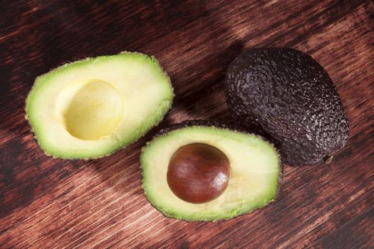 Delicious fresh ripe avocado cross section on brown wooden background, top view. Healthy fresh fruit eating.