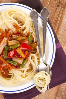 Culinary pasta eating. Pasta with tomato vegetable sauce on plate with cutlery on wooden background, top view.