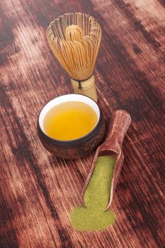 Traditional green powdered tea matcha with cup of tea, bamboo chasen on wooden background. Healthy tea drinking.