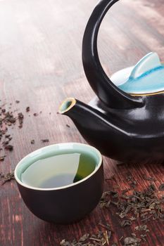 Traditional green tea ceremony. Tea in tea bowl with ceramic tea pot, dry tea crop on brown wooden background. Asian tea drinking.