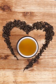 Green tea leaves in heart shape with cup of tea on wooden background. I love tea concept.