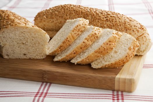 Cut white sesame baguette on wooden slab.