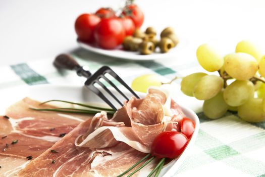 Delicious prosciutto plate with olives, tomatos and grapes.