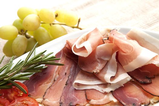 Delicious prosciutto plate with tomatos, grapes and rosemary.