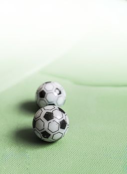 Two toy footballs in lineup on green canvas fading out to white. Vertical image with copy space.