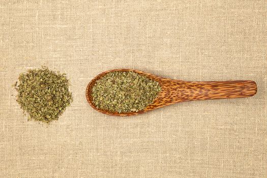 Dry marjoram spice on bamboo spoon on brown background, top view.