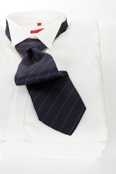 Pile of white dress shirts with red striped tie on white background. Contemporary business concept.