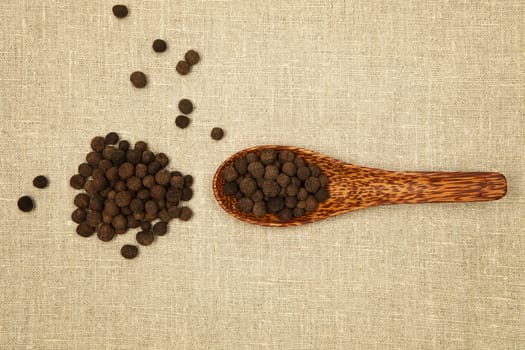 Peppercorns on bamboo spoon on brown background, top view. 