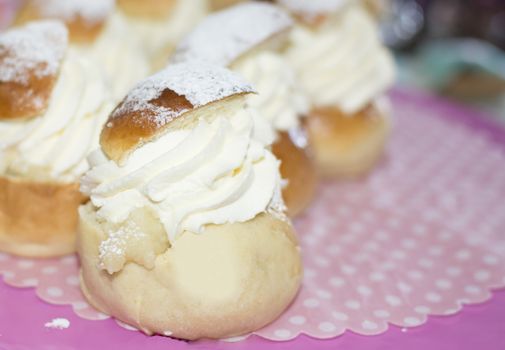 Typical Swedish buns in February - semla - with whipped cream on pink and white dotted paper and pink cakeplate.