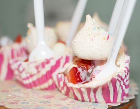 Cupcake with merengue and strawberry in paper cups and plastic spoons.