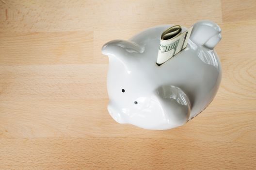 US $100 dollar bill, folded, sticking out of small white piggy bank on wooden cut board