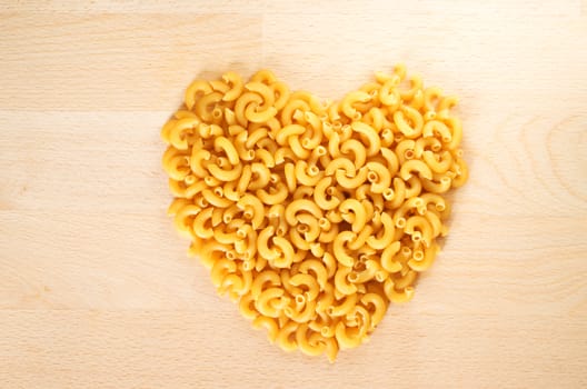 Macaroni forming a heart over a wooden cut board. Concept of healthy food. 
