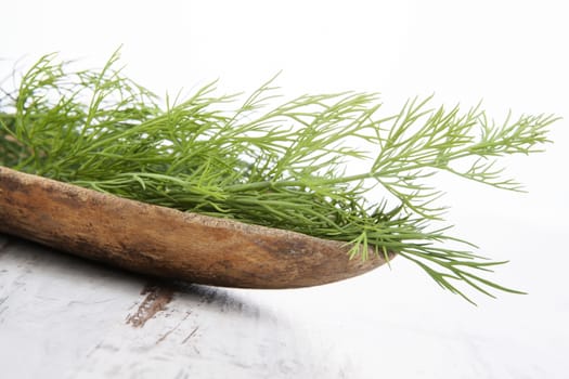 Fresh dill in wooden bowl on white wooden background. Aromatic culinary herbs, traditional rustic style.