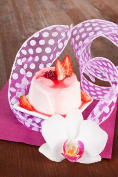 Delicious pudding with fresh strawberries and cream decorated with orchid on purple and wooden background. Culinary sweets concept.