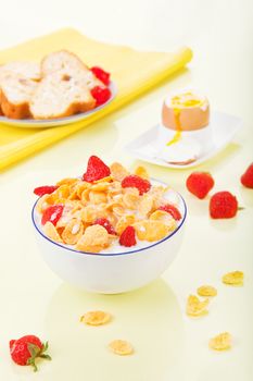Delicious fresh healthy breakfast. Corn flakes with strawberries in bowl, bread and egg in background.