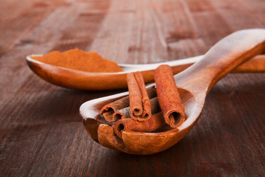 Cinnamon sticks on spoon and cinnamon powder on wooden spoon in background. Brown natural culinary spice concept.