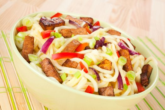 Traditional asian noodles with vegetable and tofu in green bowl on light wooden background. Asian culinary food.