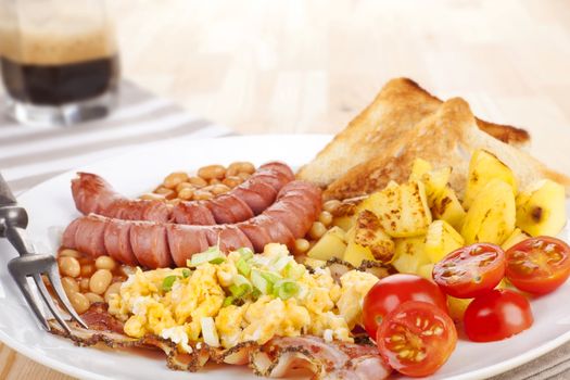 Delicious english breakfast. Beans, sausages and scrambled eggs on white plate with fork. Coffee in background. Light wooden background. Good morning concept.