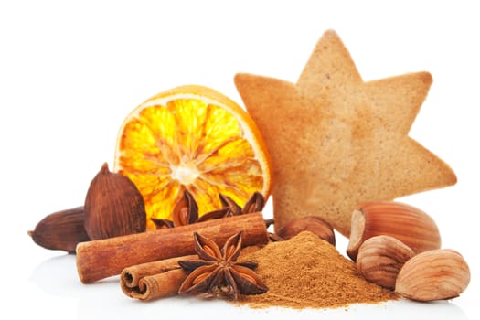 Culinary aromatic spices christmas background. Anise, cinnamon and various nuts. Star shaped gingerbread cookie and orange slice in background on white. Traditional xmas still life. 