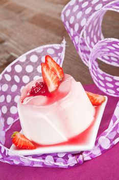 Delicious pudding with fresh strawberries and cream on purple and wooden background. Culinary sweets concept.