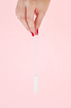 Female hand with red fingernails holding a clean tampon. Feminine hygiene concept.